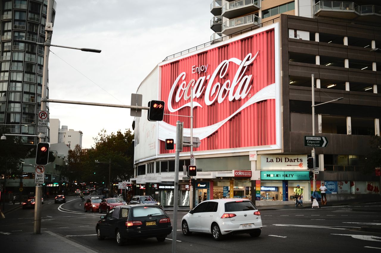 Sydneys famous Coca-Cola billboard lights up a busy street corner.
